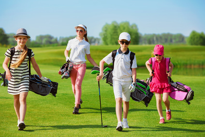 Kids walking on fairway with bags at golf school
